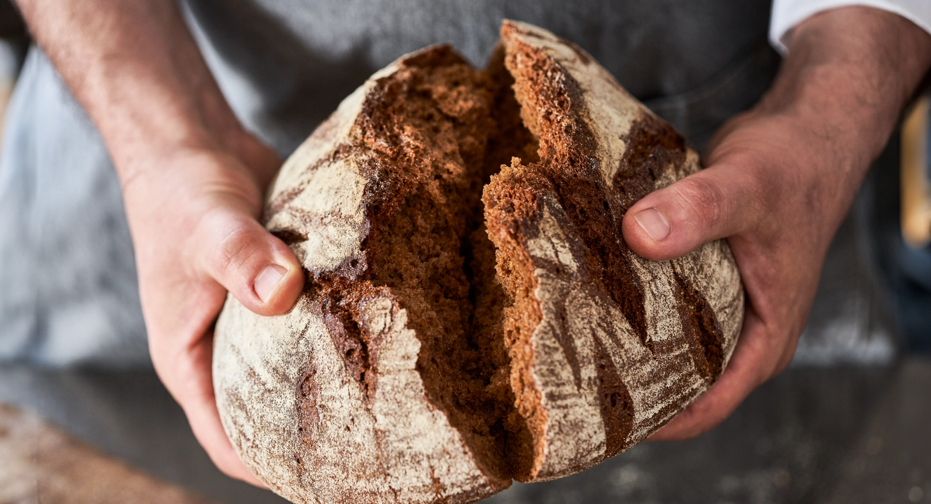 Mani di uno chef che spezzano a metà una pagnotta ai cereali