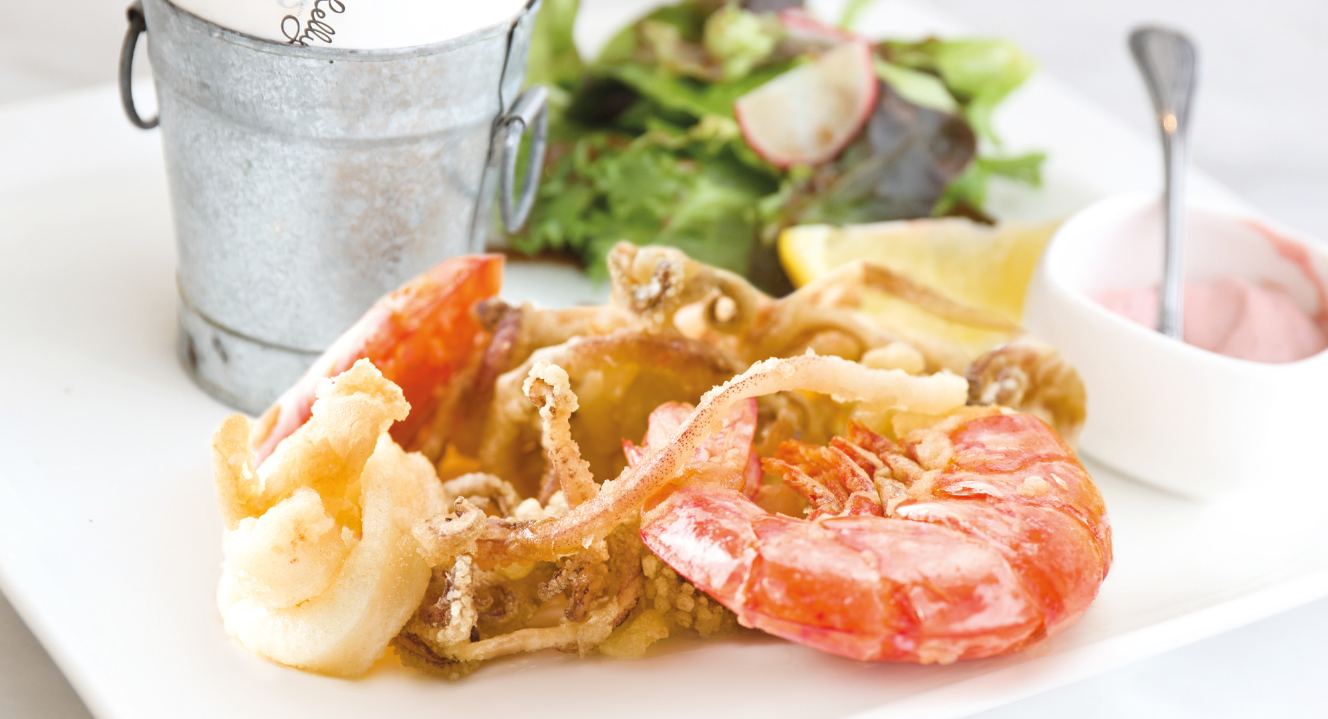 Piatto con frittura di pesce e accanto salsa di accompagnamento e insalata