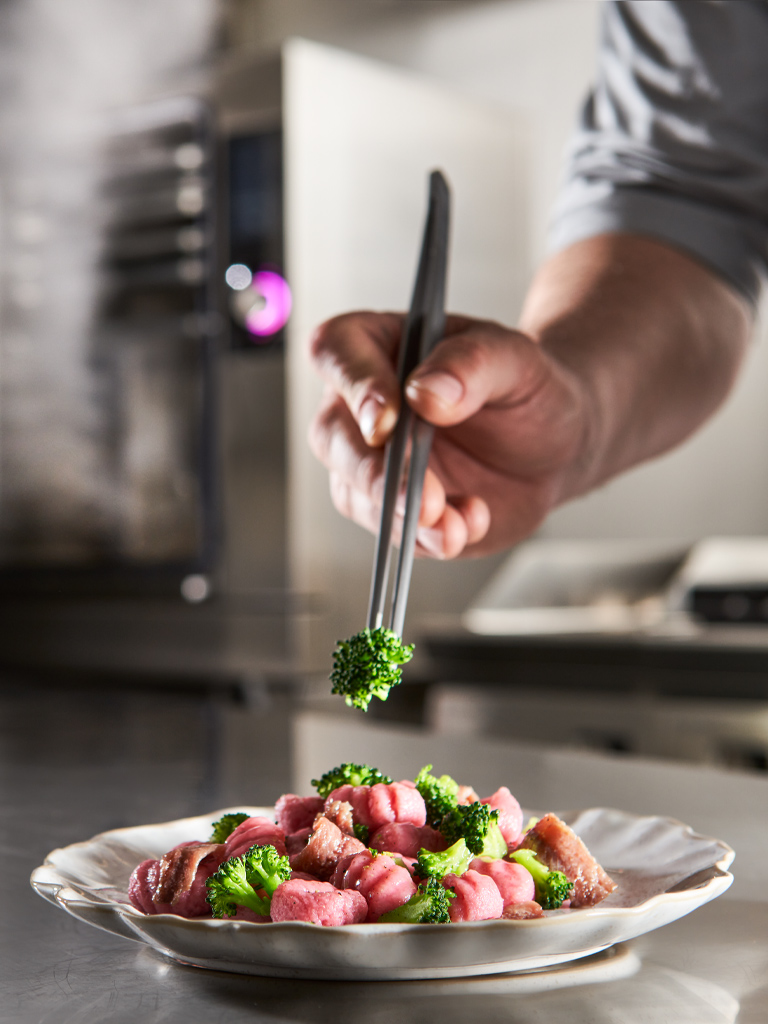 mano di uomo che impiatta un piatto appena pronto di carne e verdure