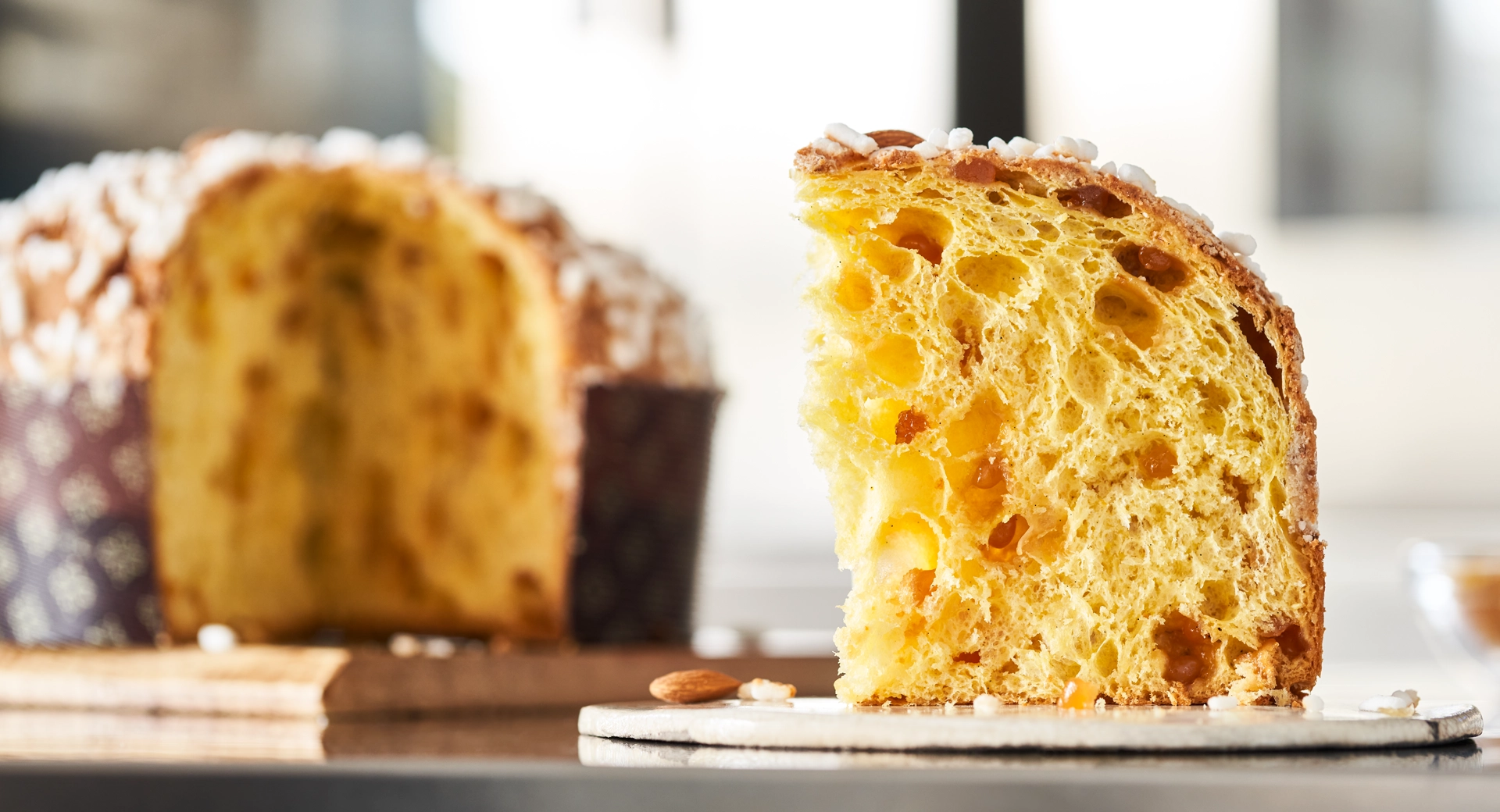 Fetta di panettone con canditi su un piatto con panettone interno sullo sfondo